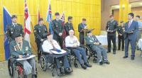 On the right, Kangjun Lee holds the citation in anticipation of presentation while the MC and President of KVA Unit 21, John McDonald reads it aloud. From left to right are: Austin McClure of 59 Independent Field Squadron, Royal Canadian Engineers, William Greeley of 2 PPCLI, Kenneth Storey of the Royal Canadian Medical Corps, and Samuel Frischkent of the Royal Canadian Army Service Corps.